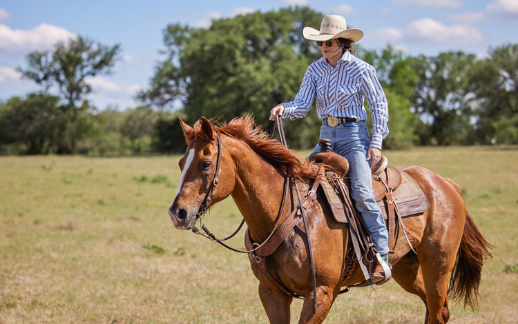 woman riding a horse wearing cowgirl attire.